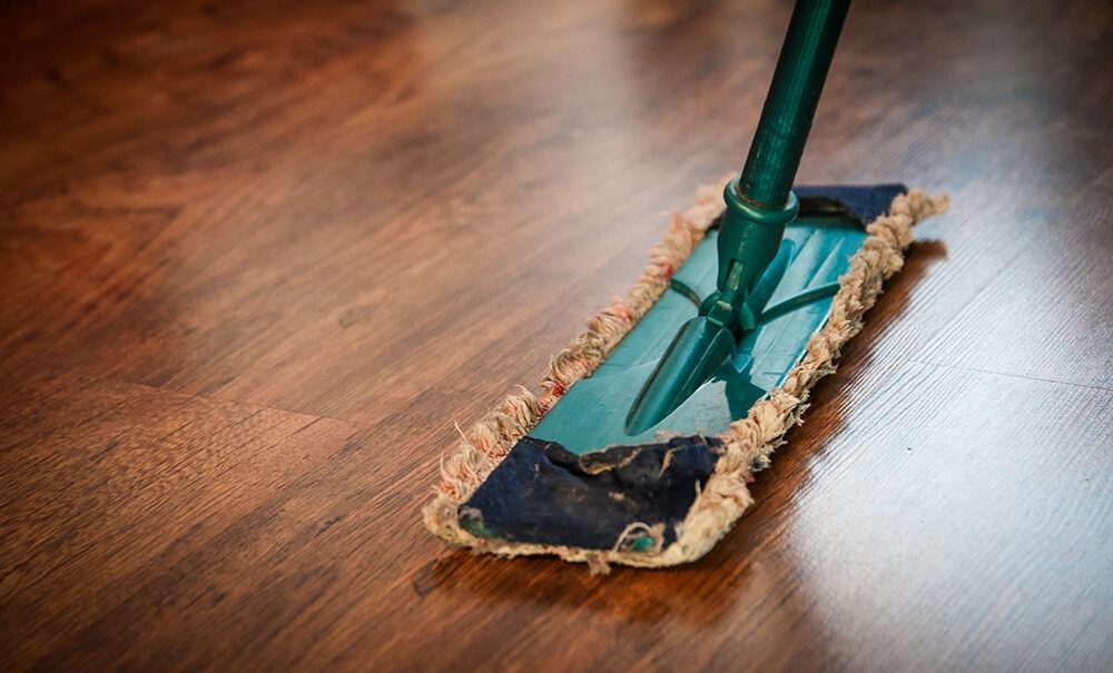 A mop cleans a dark wood floor